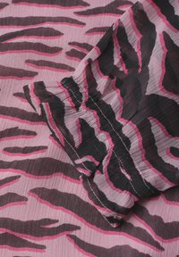 Tissu rose avec des rayures zèbre noires et rose foncé, avec un détail de couture froncée et élastique.