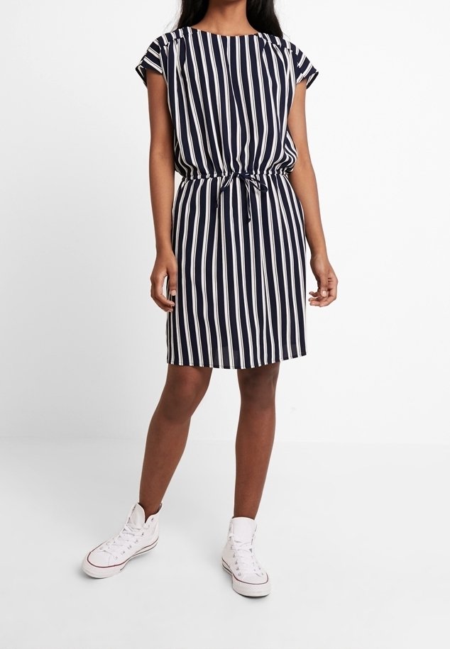 Vestido a rayas azul marino y blanco con mangas cortas, cintura fruncida y detalle de corbata. Combinado con zapatillas blancas para un look casual.