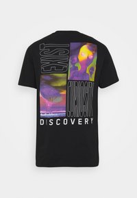 T-shirt en coton noir avec des imprimés graphiques vibrants, comprenant des aliens abstraits et des motifs de texte en tons blancs, violets et verts.