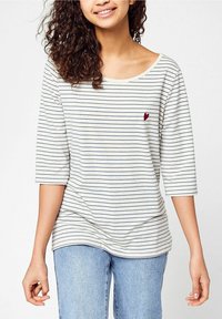 Räfflad långärmad skjorta i krämfärg och marinblå, rund halsringning, lös passform, med ett litet rött hjärtemblem på bröstet.