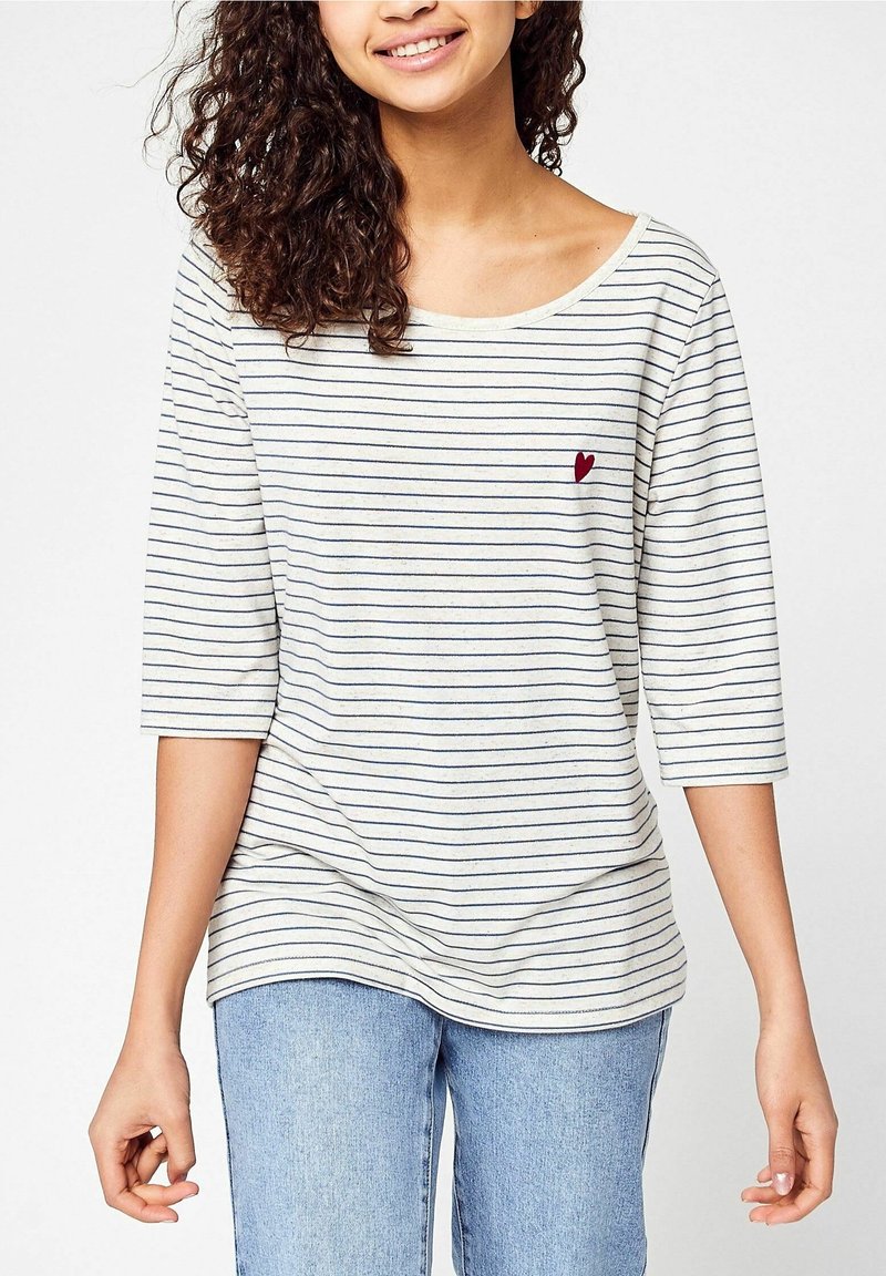 Räfflad långärmad skjorta i krämfärg och marinblå, rund halsringning, lös passform, med ett litet rött hjärtemblem på bröstet.