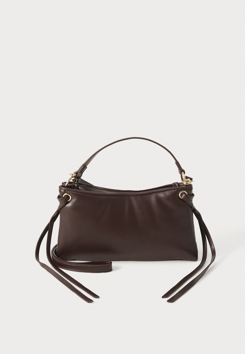 Sac à main en cuir marron foncé avec une poignée courte et de longues lanières fines attachées à travers des œillets dorés de chaque côté.