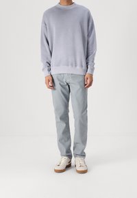 Lys grå sweatshirt med rund hals og dropped shoulders, kombineret med lyseblå denimbukser og hvide sneakers med brune såler.