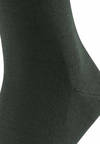 Dunkelgrüne Socke aus einem glatten, elastischen Material. Verfügt über eine gerippte Struktur und eine verstärkte Ferse. Form passt sich dem Fuß an.