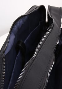 Svart tygväska med marinblå foder inuti, med en silverdragkedja längs öppningen och synliga innerfickor.