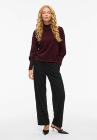 Burgundy tröja med texturerade ärmar, kombinerad med svarta, vida byxor och svarta klackmuler. Enkelt design och mjukt tyg.