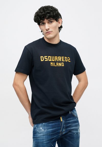 Sort bomulds-t-shirt med fed gul "DSQUARED2 MILANO" tekst, rund hals og klassisk pasform, kombineret med blå slidte jeans.