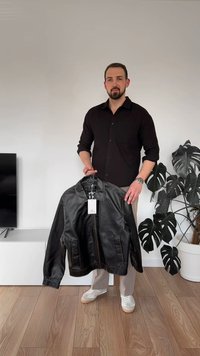 Svart läderjacka med krage, framdragkedja och två sidofickor. Slät textur med minimala sömnadsdetaljer. Hängande etikett synlig.
