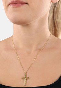 Guldhalsband med en vertikal korspendel med en detaljerad figur i mitten, bärs mot en bar nacke.