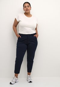 White short-sleeve t-shirt paired with navy tapered pants. Pants feature a tailored fit and side pockets. Footwear: white and grey athletic shoes.