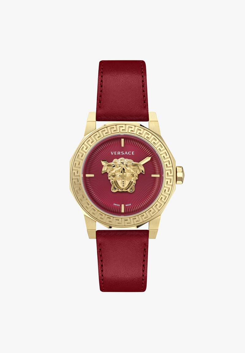 Zelta toņa astoņstūra pulkstenis ar sarkanu analogo ciparnīcu, kurā attēlota Medūzas galva, Grieķu atslēgas raksta apmale un bordo ādas siksna.