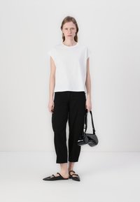 Bílý top s krátkým rukávem, černé široké kalhoty, černá lakovaná kabelka a špičaté pantofle. Jednoduchý design s čistými liniemi a neutrálními barvami.