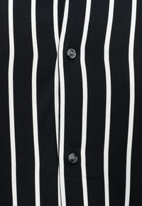 Schwarzer Stoff mit vertikalen weißen Streifen und zwei sichtbaren schwarzen Knöpfen, Nahaufnahme der Vorderseite eines gestreiften Hemdes.