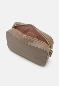 Pochette en cuir beige avec une finition texturée, fermeture éclair dorée et intérieur marron. Présente un design arrondi adapté aux petits essentiels.