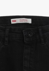 Jeans Levi's 720 de talle alto y súper ajustados en denim negro. Presentan cierre de botones, presillas para cinturón y un acabado texturizado.