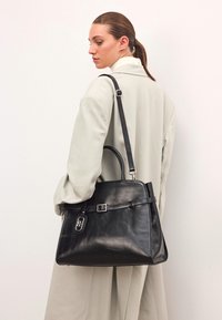 Melna ādas rokassoma ar strukturētu formu, augšējām rokturiem, regulējamu pleca siksnu un metāla apdari. Gluda tekstūra.