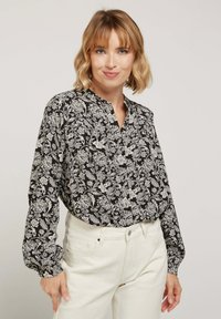 Blouse florale en noir et blanc avec un col mandarin et des manches longues, présentant une coupe ample et un motif botanique détaillé.