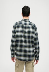 Langermet rutet skjorte med marineblå, hvite og gule striper. Knappede mansjetter, klassisk krage og rett kant. Brukt med khaki-bukser.