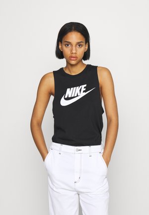 Canotta nera senza maniche Nike con logo bianco, abbinata a pantaloni bianchi a vita alta con cuciture visibili e chiusura con bottone.