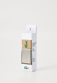 Cinturón Lacoste en tela marrón con hebilla de metal plateado; presenta el logo del cocodrilo verde y texto en el embalaje. Diseño ligero y duradero.