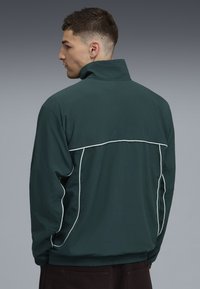 Dunkelgr�üne Windbreaker-Jacke mit hohem Kragen, elastischen Bündchen und kontrastierenden weißen Paspeln entlang der Schultern und Seiten.