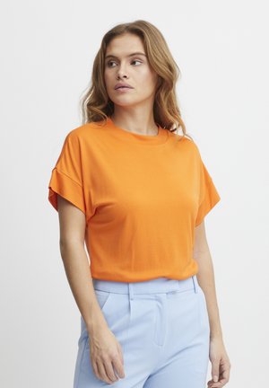 Orange kortärmad t-shirt med rund halsringning och lös passform, kombinerad med ljusblå byxor i mjukt bomullsmaterial.
