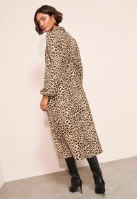 Midi obleka s leopardjim vzorcem iz lahkega materiala, z dolgimi puhastimi rokavi in cinčanim pasom, v kombinaciji s črnimi škornji do kolen.
