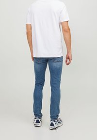 Vit bomulls-t-shirt som bärs med blå denimjeans. Jeansen har slim fit och har bakfickor samt en blekt finish. Vita och marinblå sneakers.