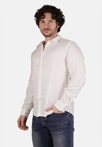 Camicia bianca di lino a maniche lunghe con chiusura a bottoni, texture morbida e colletto classico, abbinata a jeans blu scuri.