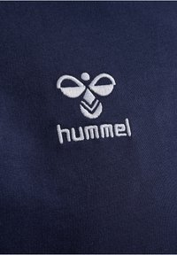 Mörkblått tyg med en vit broderad logotyp som liknar en bi och ordet "hummel" nedanför, med en slät yta.