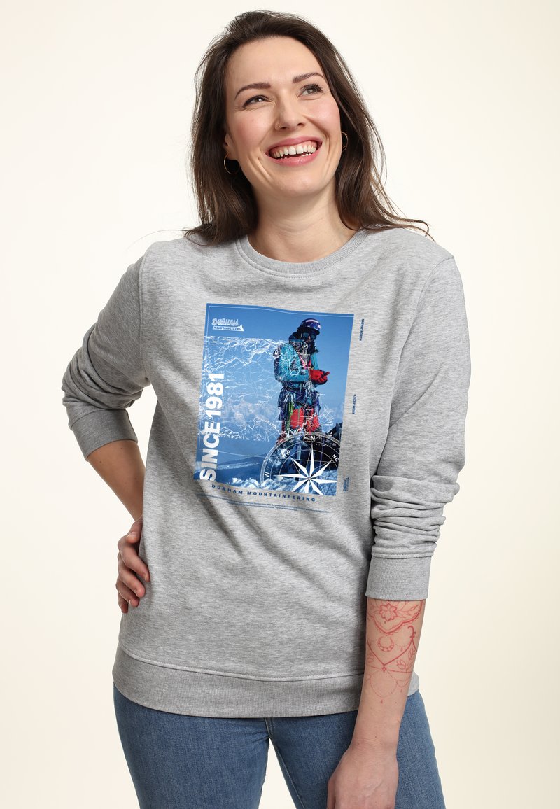 Felpa grigia con una grafica blu di un alpinista, "SINCE 1981," e un design a forma di bussola. Tessuto morbido con polsini e orlo a costine.