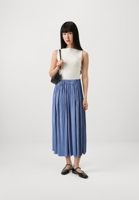 Hvit ribbet tanktopp kombinert med et midtlengdes blått plisséskjørt. Modellen holder en liten svart crossbody-veske, og har på seg svarte flate sko.