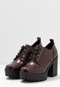 Chaussures à plateforme en cuir de crocodile marron avec une épaisse semelle noire, un design à lacets et un bout arrondi. Présente des œillets en argent et une hauteur chevillère.