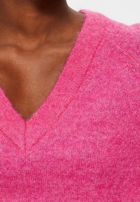 Close-up van een persoon die een levendig roze v-hals trui draagt, met een zachte textuur en een nette halslijn tegen een neutrale achtergrond.