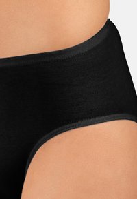 Mutande nere a vita alta con costine indossate sul torso inferiore e sui fianchi su uno sfondo neutro.