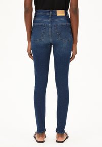 Hoch taillierte dunkelblaue Jeans mit glatter Textur, Gesäßtaschen und einem Lederlabel auf dem Bund. Figurbetontes und schmal zulaufendes Design.