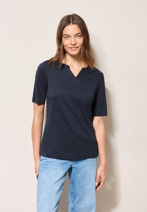 Haut bleu marine à manches courtes avec un col en V et des détails de couture, fabriqué dans un tissu lisse. Associé à un jean en denim bleu clair à coupe décontractée.