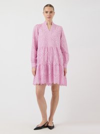 Ružičasta pamučna haljina s visokim izrezom, dugim rukavima i oštrim rubom. Isečeni detalji stvaraju uzorke kroz tkaninu.