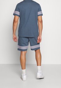 Pánská sportovní souprava v tmavě modré barvě, obsahující tričko s krátkým rukávem a rukávy se růžovými pruhy a odpovídající šortky se stejnými pruhy.