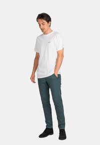 Camiseta blanca de algodón con mangas cortas y un pequeño logo en el pecho, combinada con pantalones verde oscuro y zapatos negros.