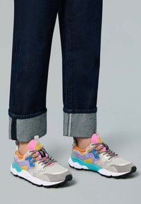 Sneakers colorati con una combinazione di suede grigio, blu, arancione e viola, con suole nere e lacci a contrasto. Visibili jeans in denim con risvolto.