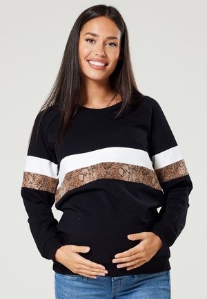 Sort sweatshirt med hvide og slange-mønstret vandrette striber. Har en rund halsudskæring og lange ærmer, lavet af blødt stof.
