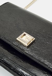 Svart texturerad läderclutch med ett fyrkantigt guldtonat spänne prytt med strass, som har en slimmad design och kedjerem för att bära.