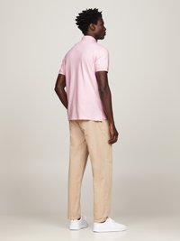Roze polo met korte mouwen en beige broek, vergezeld van witte sneakers. De polo heeft een klassieke kraag en een relaxte pasvorm.