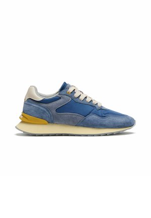 Blauwe en grijze suède sneaker met beige veters, gele hielaccent en off-white zool, zijaanzicht op witte achtergrond.