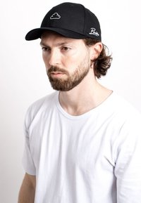 Black cap with white cloud design on front and script logo on the side, worn with a plain white t-shirt. Fabric appears smooth and structured.