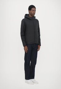 Schwarze Zip-Jacke mit Kapuze, mit glatter Textur und elastischen Bündchen. Kombiniert mit dunkelblauen Jeans und weißen Sneakers.