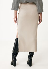 Beige ribbad midikjol med sidofår, knapprande detaljer, matchad med svarta knähöga stövlar, visad mot en vit bakgrund.