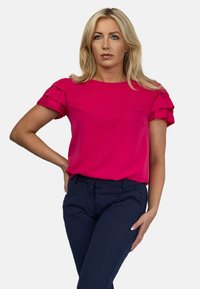 Fuksjowa bluzka z falbaniastymi krótkimi rękawami, parowana z ciemnonawowym spodniami z subtelnym wzorem w kropki. Prosty dekolt i luźny krój.