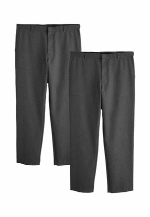 Mężczyzna z warkoczami, ubrany w czarną kurtkę w plamki, jasnoniebieską koszulę, szare spodnie i czarne buty, stojący na białym tle.